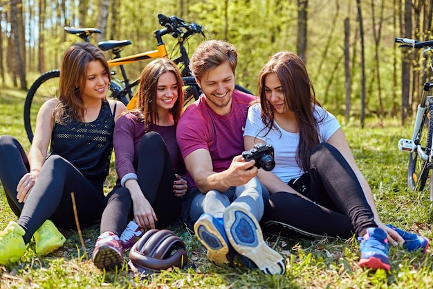 Бесплатное фото Группа людей просматривает фотоснимки на компактные фотоаппараты и отдыхает после велопрогулки в лесу.