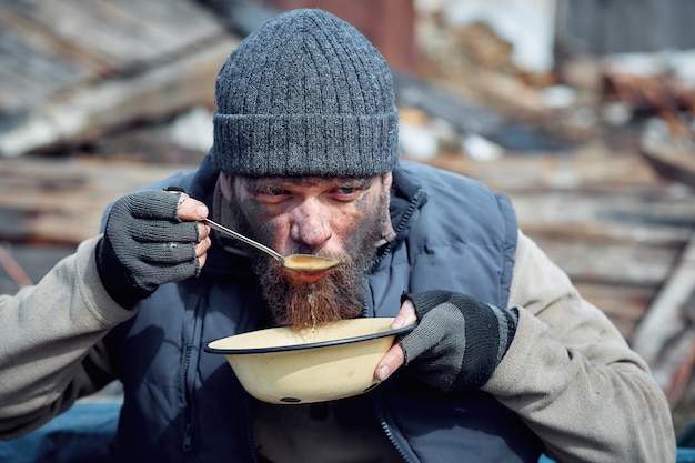 ホームレスの男性が廃墟の近くの皿からスープを食べ 伝染病の最中に貧困層と飢えた人々を助ける プレミアム写真