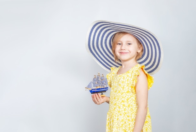 챙이 넓은 모자에있는 어린 백인 소녀는 그녀의 손에 장난감 보트를 보유하고 있습니다. 여름 휴가의 개념