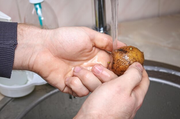 한 남자가 생 감자를 싱크대에서 물로 씻고 오븐에서 호일에 굽는다