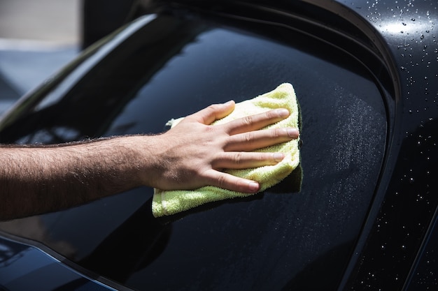 한 남자가 젖은 차를 걸레로 닦는다.