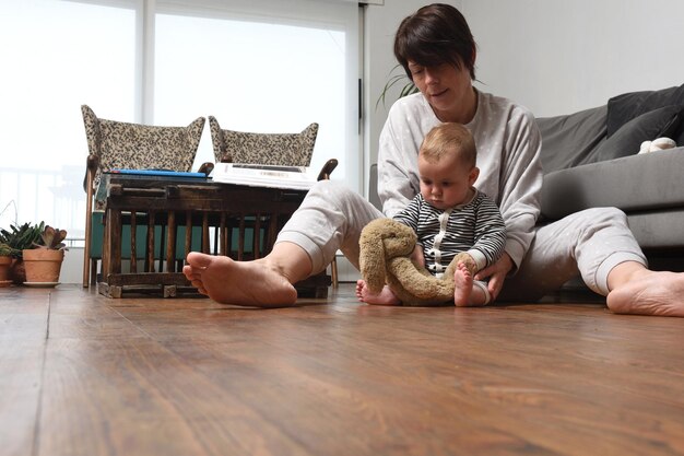 赤ちゃんが人形で遊んでいる家の木の床に赤ちゃんを持つ母親