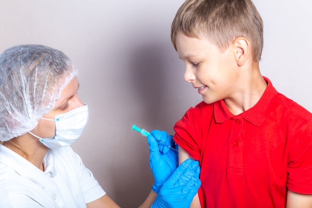 マスク​と​青い​手袋​を​着用した​看護師​が​注射器​から​男の子​に​ワクチン​を​注射します