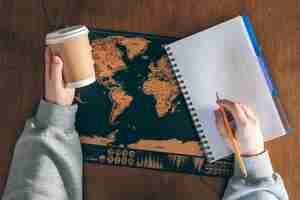 무료 사진 여자 손 에 있는 종이 컵, 빈 노트북, 나무 테이블 에 있는 세계 지도
