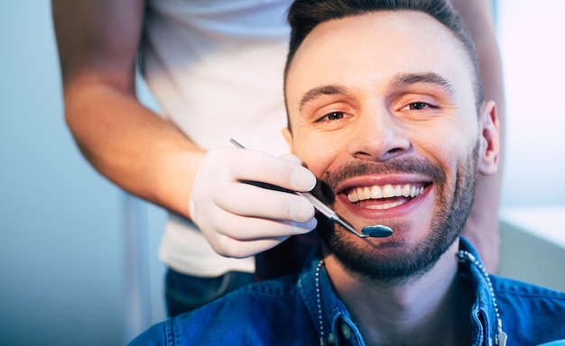 クリニック​で​行われた​治療​の​結果​に​完全​に​満足している​患者​の​美しく​白い​笑顔​で​見られる​歯科医​の​仕事​の​完璧な​結果