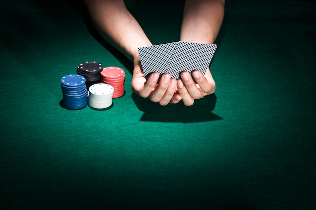 カジノのテーブルにポーカーチップのスタッキングとトランプを持っている人の手