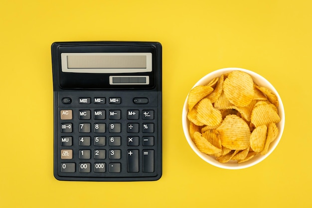 Бесплатное фото Тарелка картофельных чипсов и калькулятор на желтом фоне сверху