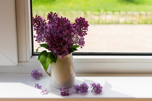 白い​水差し​の​ライラック​の​紫色​の​花束​は​、​カントリー​ハウス​の​窓辺​に​立っています​。