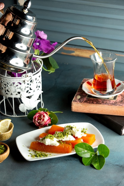 Бесплатное фото Порция айвового десерта со сливками и фисташками, подается с черным чаем