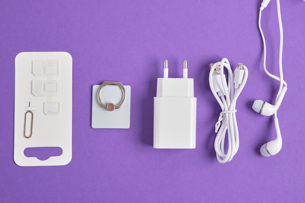 スマートフォン、充電器、ヘッドフォン、リングを保持するためのアクセサリのセット、紫色の背景のコピースペースの上面図にsimカード用のアダプター Premium写真