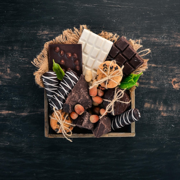Набор молочного шоколада и черного шоколада в деревянной коробке с орехами и печеньем на черном деревянном фоне скопируйте место для текста Premium Фотографии