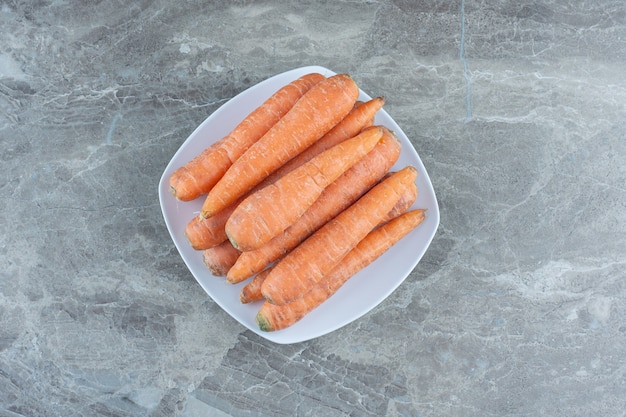Стопка моркови в тарелке на мраморном столе.