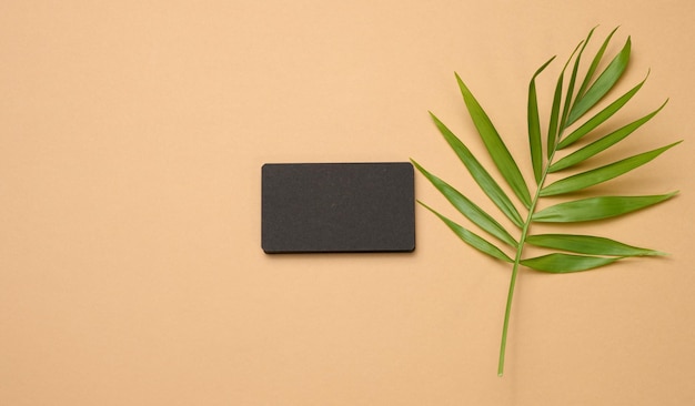 Стопка прямоугольных визитных карточек из черной бумаги и лист пальмы на коричневом фоне. вид сверху, современный шаблон для фирменного стиля
