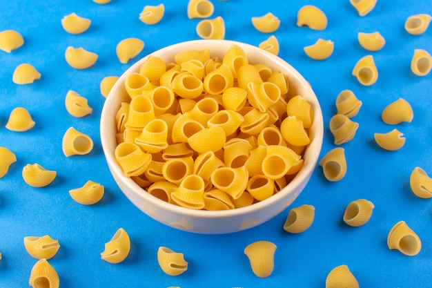 Бесплатное фото Вид сверху итальянская сухая паста, образованная маленькой желтой сырой пастой внутри круглой миски кремового цвета, изолированная на синем фоне итальянская паста для спагетти