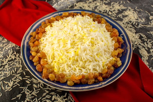 Бесплатное фото Вид сверху вкусного плова с маслом и изюмом внутри тарелки с сырым рисом на темной поверхности