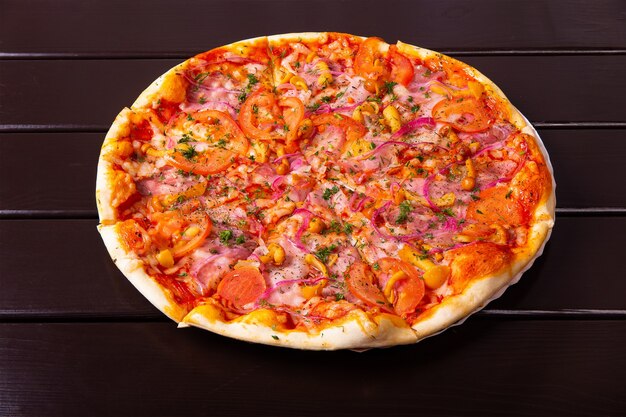 モッツァレラチーズ、ブリスケット、ハム、トマト、赤玉ねぎ、ハニーデューを添えた素朴なピザを木製のテーブルの紙皿に盛り付けます