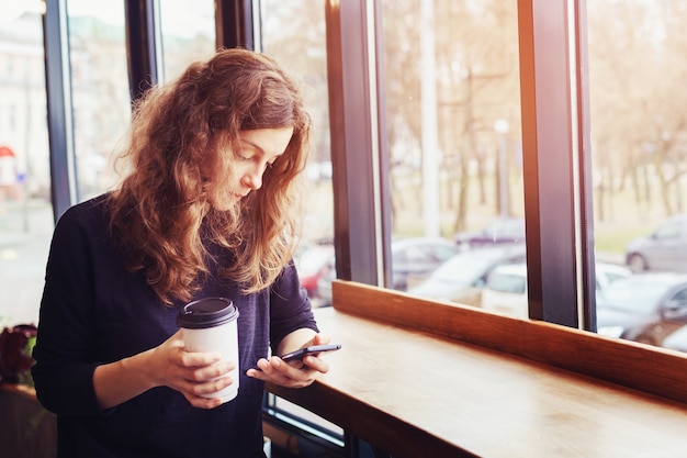 女性がカフェでコーヒーを飲み、電話を使う Premium写真