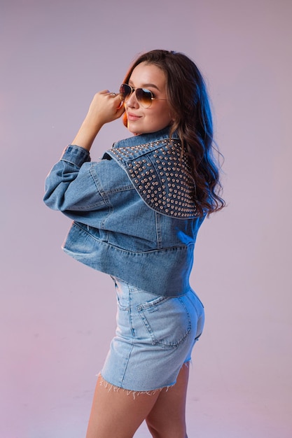 Бесплатное фото Женщина в солнцезащитных очках джинсовых шорт в студии на интересном красивом фоне