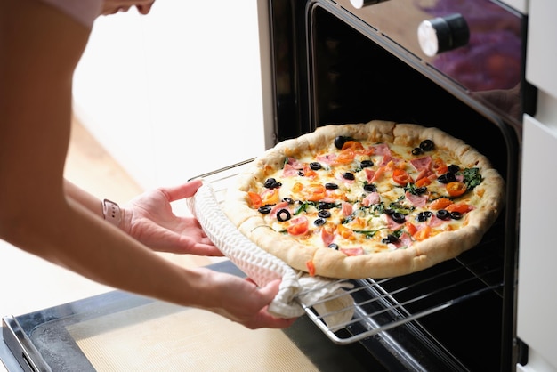Женщина достает пиццу из духовки крупным планом руками