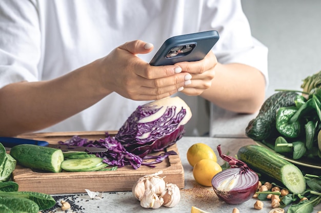 無料写真 女性がキッチンでスマートフォンを使って野菜サラダを準備している