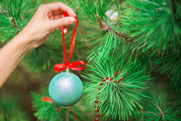 女性の手が松の枝に赤いリボンでクリスマスボールを掛ける
