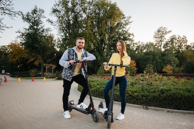 暖かい​秋​の​日に​、​若い​美しい​カップル​が​公園​で​電動​スクーター​に​乗ります​。​趣味​と​レクリエーション​。