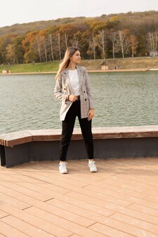 Молодая красивая девушка в сером пиджаке стоит на набережной реки осенний городской парк