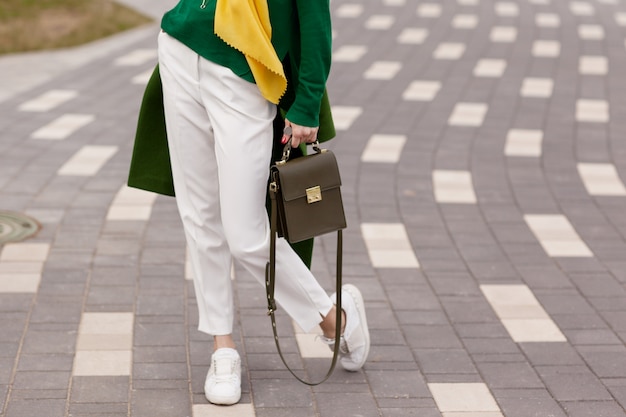 Молодая девушка в белых брюках, теплая зелень пальто Premium Фотографии