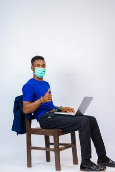 흰색 배경에 격리된 젊고 잘생긴 아프리카 기업은 사회에서 발병하는 것을 방지하기 위해 얼굴 마스크를 쓰고 자신의 노트북에서 본 것에 흥분을 느낍니다
