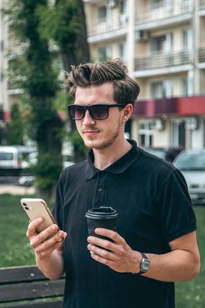 무료 사진 도시에서 스마트폰과 커피를 들고 선글라스를 쓴 청년