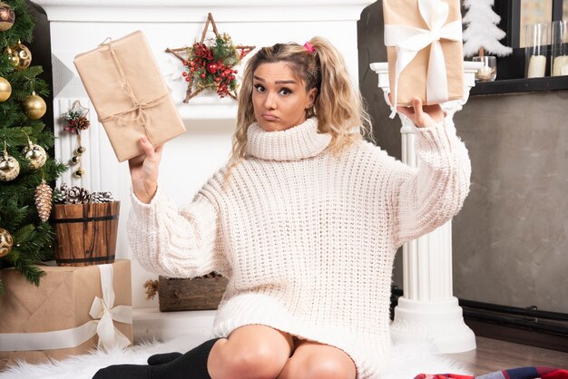 Бесплатное фото Молодая женщина в белом свитере показывает две коробки рождественских подарков.