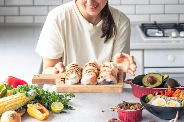Бесплатное фото Молодая женщина с блинчиками с начинкой в рисовой бумаге на кухне