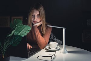 Молодая женщина работает ночью за ноутбуком при свете лампы