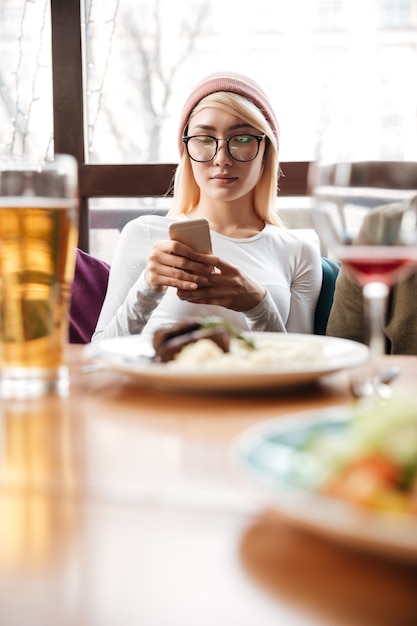 Aattractive woman sitting in cafe while using mobile phone