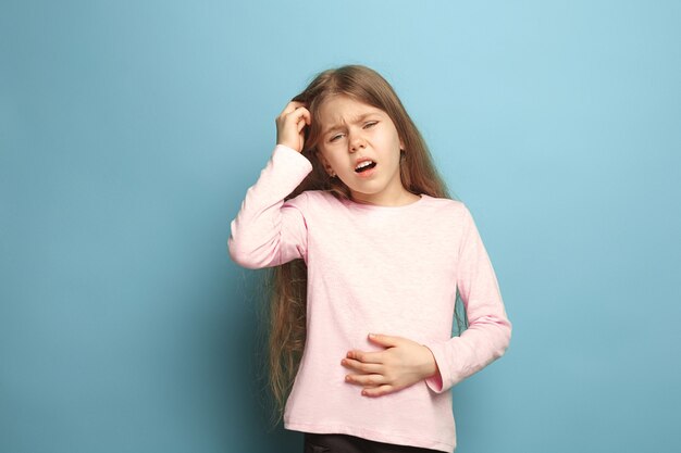 The abdominal pain. The sad teen girl with abdominal pain on a blue studio background. Facial expressions and people emotions concept. Trendy colors. Front view. Half-length portrait