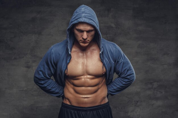 Abdominal strong man in a blue hoodie on a grey background.