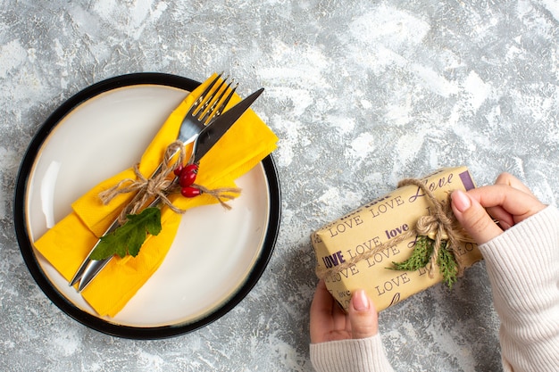 Бесплатное фото Выше вид набора столовых приборов для еды на белой тарелке и руки, держащей красивый упакованный подарок на поверхности льда