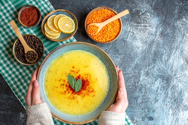 Бесплатное фото Выше вид руки, держащей синюю тарелку с вкусным супом, подаваемым с мятой и перцем на зеленом полосатом полотенце