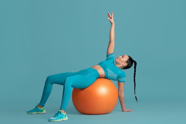 ABS training. Beautiful young female athlete practicing in studio, monochrome blue portrait