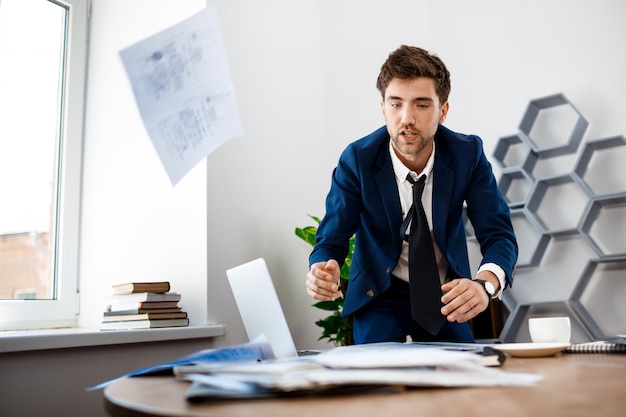 Free photo absentminded young businessman  rummaging in papers, office background.