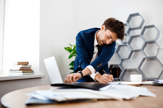 Absentminded young businessman speaking on phone, office background.