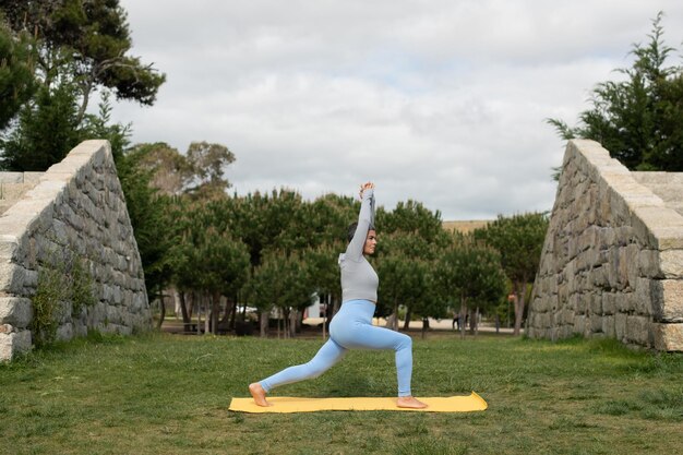 Absorbed elderly woman doing yoga in park. Female model with short gray hair exercising on mat on cloudy day. Sport, hobby, health concept