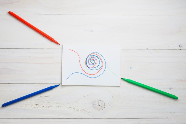 Abstract drawing on white paper with red; green and blue felt tip pen over wooden desk