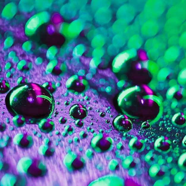 Abstract water drops on transparent purple and green glass background