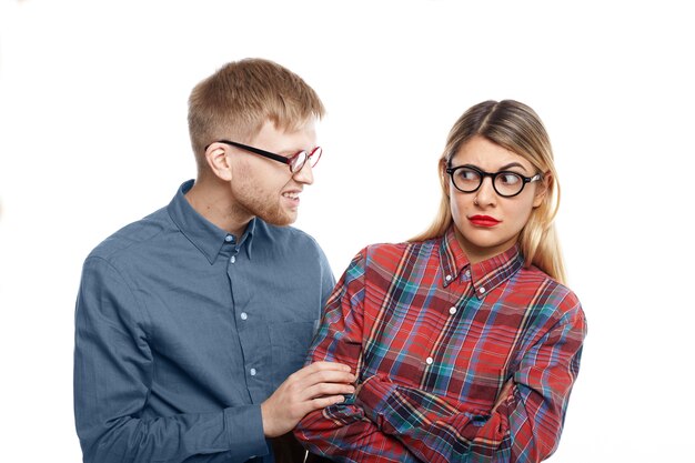 Abusive young man with stubble trying to intimidate blonde woman in checkered shirt, pulling her by sleeve. Caucasian female being abused by bearded male, looking at him with eyes full of terror