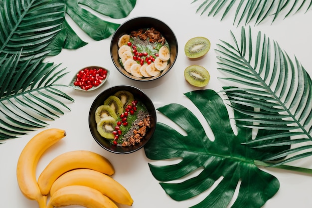 Free photo acai bowl with healthy berries, kiwi, avocado  on tropical palm leaf. healthy vegetarian food.