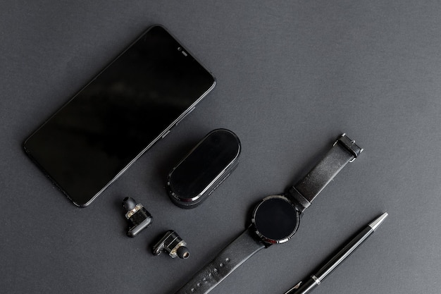 단색 배경에 남성의 아름다움을 위한 액세서리. 검은색 펜, 검은색 스마트 시계, 스마트폰, 그리고 어두운 배경의 무선 헤드폰. 위에서 볼 수 있습니다. 미니멀리스트 블랙 트렌드 2020. 프리미엄 사진