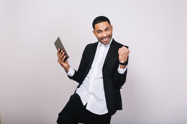 Achieving great results at work, success in career of handsome young man in white shirt, black jacket expressing happiness. Stylish businessman, modern, joyful, smiling.