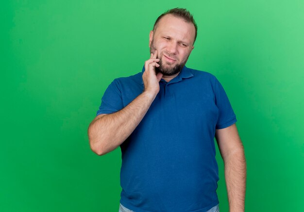 Больной взрослый славянский мужчина, смотрящий на боковую щеку, страдающий от зубной боли, изолирован на зеленой стене с копией пространства