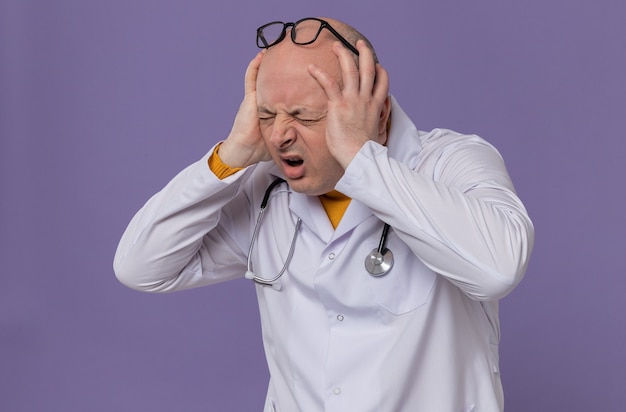 Больной взрослый славянский мужчина в очках в униформе врача со стетоскопом, положив руки ему на голову